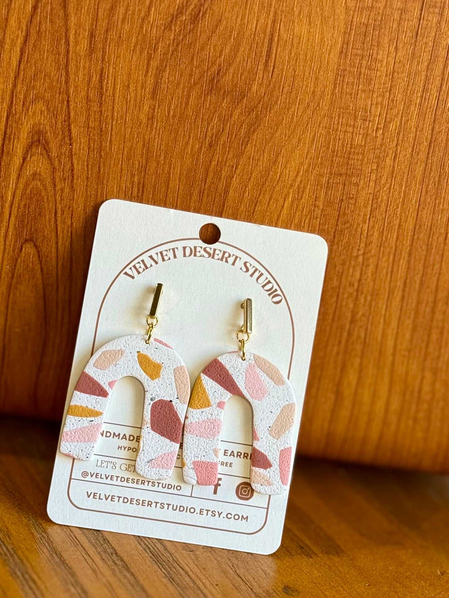 Pair of earrings on a Velvet Desert Studio card against a wooden background