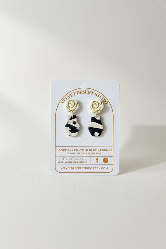 pair of vase earrings with rose shaped tops on a velvet desert studio product backing card on a white background.