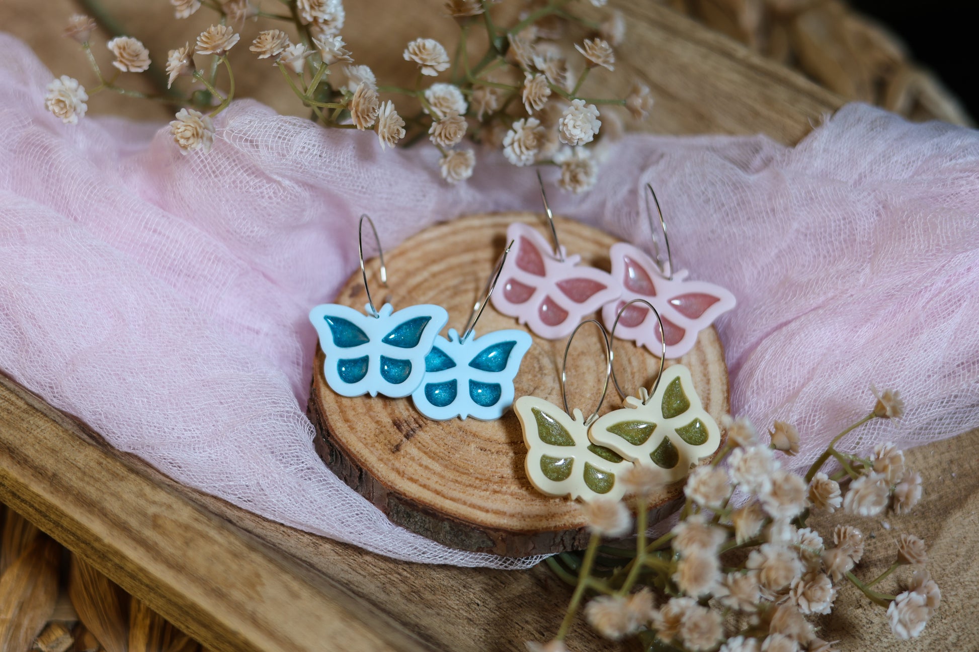 Butterfly-shaped earrings on a wooden slice with dried flowers