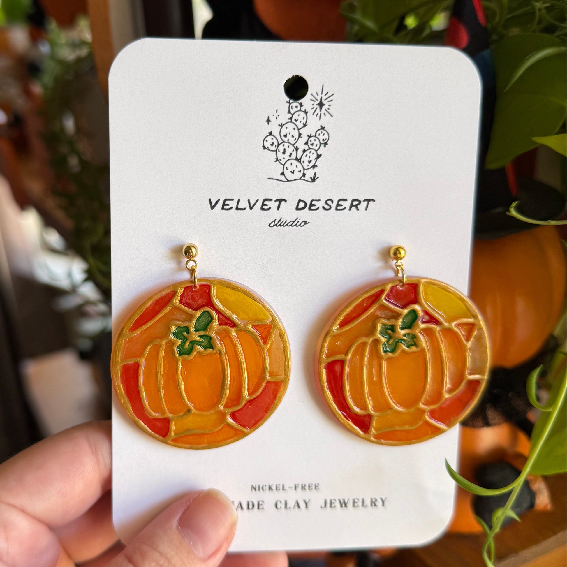 Hand holding a card with pumpkin-shaped earrings on a blurred background